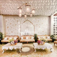 A sophisticated lounge area designed with a palette of white, cream, and gold. The decor features elegant vintage-style furniture, a custom-printed floral wallpaper, and a stunning ceiling treatment with ruffled fabric.