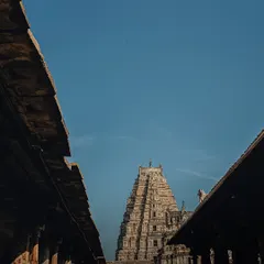 A low-angle shot looking up at the gopuram (tower) of the Virupaksha Temple, framed by the roofs of the surrounding structures. The composition emphasizes the temple's towering height and intricate carvings.
