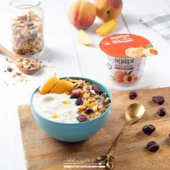 A creamy bowl of peach-flavored yogurt. The bright, airy lighting and fresh peach slices clearly communicate the flavor and the product's fresh quality.