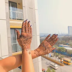 This design prominently features parrots, a popular motif in bridal and festive henna. The way the hands are held up against the sky really shows off the detailed line work.