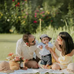 A family enjoying a picnic setup in a park. This shot captures a candid moment as the parents interact with their curious baby.