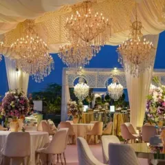 An elegant evening reception setup under a draped canopy, illuminated by dozens of magnificent crystal chandeliers. The pastel color scheme and sophisticated table settings create a luxurious and timeless atmosphere for a large gathering.