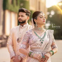 A regal portrait of the couple. The groom's pastel sherwani with a matching dhoti is adorned with a pearl necklace, creating a look of modern royalty against the palace backdrop.