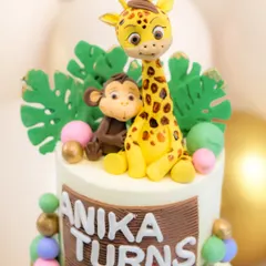 A close-up of the top tier, showing the detailed, hand-sculpted fondant giraffe and monkey among tropical leaves.