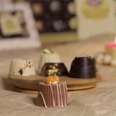 Showcasing the variety in our soft-center chocolate collection. In focus is the caramel-filled milk chocolate piece, with other flavors like tiramisu, pista kunafa, and roasted almond visible in the background.
