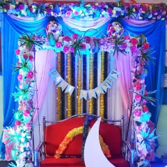 A close-up of a decorated swing for a baby shower. The frame is wrapped in colorful flowers and lights, with a "Baby Shower" banner hanging in the background.