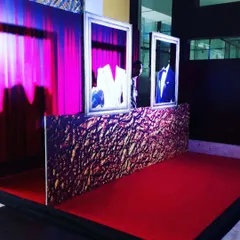 A unique photo booth or display area I designed for a formal event. It features mannequins in suits inside picture frames, set against a textured gold wall, red carpet, and dramatic purple curtain.