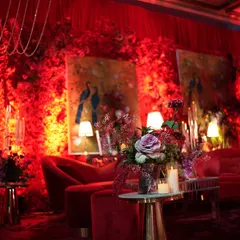 Another view of the red-on-red lounge, highlighting the rich textures of the floral walls and the elegant seating. Floor lamps and table lamps cast a soft, intimate glow, making the bold space feel warm and inviting.