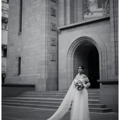 The timeless elegance of a bride. This portrait, shot in classic black and white, highlights the serene beauty and anticipation before the ceremony, showcasing our artistic approach to bridal photography against a stunning architectural backdrop.