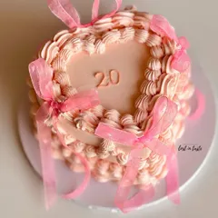 A beautiful heart-shaped cake in a soft pink hue, decorated with classic vintage Lambeth piping and delicate organza ribbons. This design is perfect for celebrating a 20th birthday in style.