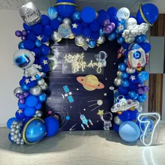 An out-of-this-world space theme birthday party for a 7-year-old. This detailed setup includes a galaxy backdrop, a full balloon arch in shades of blue and silver, and fun foil balloons shaped like astronauts, rockets, and planets.