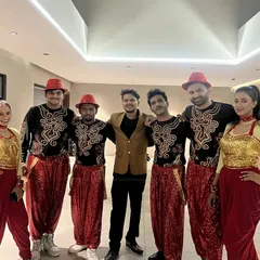 Our team of male and female dancers in vibrant red and yellow folk-inspired costumes, posing with our lead choreographer backstage before a performance.