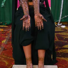 A complete bridal look, showing the intricate mehndi on both hands and feet. The feet feature a simple yet elegant design that complements the heavy work on the arms.
