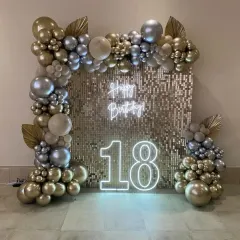 An 18th birthday photo booth featuring a gold sequin wall, a neon sign, a light-up "18", and a balloon arch in metallic shades of gold and silver.