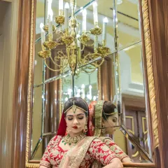 A classic bridal portrait, with the bride looking at her reflection in an ornate mirror, a grand chandelier adding to the luxurious feel.
