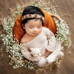 A peaceful newborn nestled in a rustic basket, surrounded by baby's breath and holding a tiny teddy. These posed shots are perfect for capturing their angelic features.
