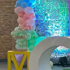 A detail shot of a party corner, showing a crescent moon prop and a decorative birdcage next to a shimmer wall and pastel balloons.