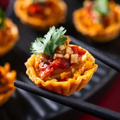 A perfect single bite of our Satay Chicken Phyllo Cups. The flaky, buttery phyllo shell holds tender satay chicken, creating a delightful contrast of textures and flavors that is both elegant and satisfying.