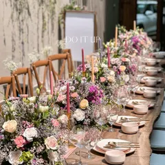 A long-table setup for an intimate bridal shower. The wooden table is adorned with a dense runner of pink and purple flowers, creating a lush and luxurious feel for the celebration.