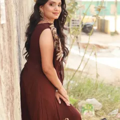 A side profile of the maroon draped gown, showing the elegant fall of the fabric and the gold leaf-pattern embroidery on the shoulder.