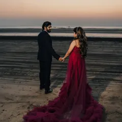 A romantic beach photoshoot at sunset. The deep red trail gown adds a touch of passion and elegance, flowing beautifully on the sand.