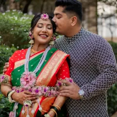 A sweet, candid moment between the couple during their baby shower photoshoot. The dad-to-be gives his wife a gentle kiss, surrounded by lush greenery.