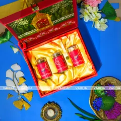 A luxurious red and gold gift box designed for wedding favors. The interior, lined with golden satin, holds three jars of flavored nuts, while the lid features a custom monogram and traditional elephant artwork.