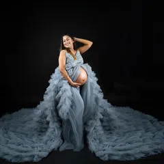 This dusty blue ruffled gown creates a spectacular circular train, perfect for a dramatic full-body portrait. The open-front design beautifully showcases the baby bump against a classic dark backdrop.