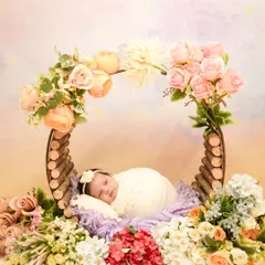 A baby rests in a rustic wooden prop adorned with a colorful mix of flowers. This setup creates a vibrant, garden-like feel for the newborn portrait.