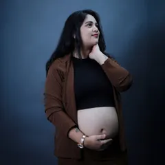 A thoughtful and modern studio portrait. The simple dark background and contemporary outfit put the focus on the mother-to-be's beautiful baby bump and serene expression.