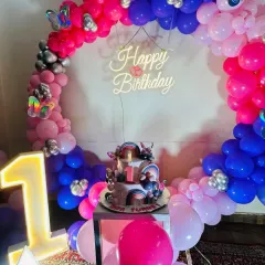 The centerpiece of the butterfly theme: a circular balloon arch in pink, purple, and blue with a 'Happy Birthday' neon sign and a light-up number '1'.
