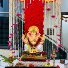 This elegant Ganpati setup uses a vibrant red floral backdrop contrasted with hanging strings of white flowers and purple accents. It's a rich and traditional look for home celebrations.