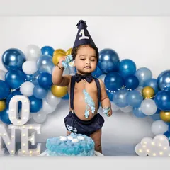 A baby boy stands proudly next to his first birthday cake, a little bit of frosting already on his hand and face. This shot captures the beginning of a fun and messy celebration.