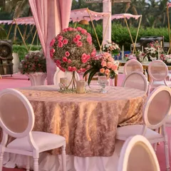 A beautiful dining setup for the beach wedding, featuring round tables with textured pink tablecloths, elegant white chairs, and stunning floral centerpieces, all set against a backdrop of palm trees.