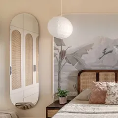 A serene bedroom view where a large oval mirror reflects the custom cane-detailed wardrobe, expanding the sense of space. The nature-inspired mural and paper lantern pendant add layers of softness and tranquility.