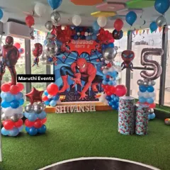 A grand Spiderman setup for Shivansh's 5th birthday. It includes a large themed backdrop, balloon columns with Spiderman figures, and a large number '5' foil balloon, all set on a green turf floor.