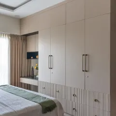 The bedroom includes a full wall of custom wardrobes with a built-in study nook. The fluted texture on the lower drawers and brass handles add a layer of refined detail.