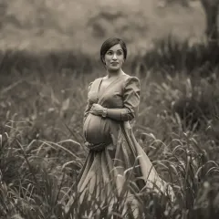 A soft and poetic black and white outdoor portrait. The expecting mother stands in a field, the monochrome finish giving the image a classic, almost historical feel.