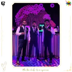 Our bartending crew posing in front of a vibrant, floral-topped bar. We are always ready to serve with style and a positive attitude.