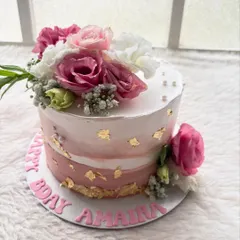 A beautiful birthday cake with a watercolor effect in shades of pink, accented with gold leaf and a crown of fresh flowers. It's both modern and timeless.