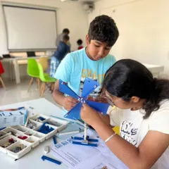 We love seeing our students collaborate and learn from each other. Two young engineers are working together to build a wind-powered machine, learning about gears and energy transfer during our hands-on summer camp.