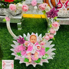 For a baby shower, I created this custom platter featuring a baby doll in a pink robe, nestled in a decorative floral cradle. This is an example of the themed and personalized decorations I offer for seemantham ceremonies.
