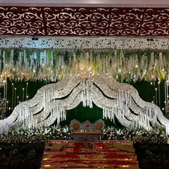 For this modern reception stage, I designed a beautiful arch made of shimmering white crystals over the main seating area. The backdrop is a simple green wall, which makes the crystal arch and the hanging floral arrangements stand out.
