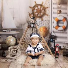 Ahoy, matey! This little sailor is ready to set sail in our nautical-themed studio setup, featuring a sailboat, ship's wheel, and fishing nets for a seafaring adventure.