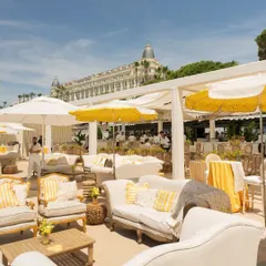 A wide view of the Mehendi lounge setup in Cannes, with white sofas, yellow-striped cushions, and umbrellas, all overlooking the beautiful beach.
