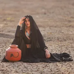 A conceptual photoshoot featuring a model in a simple yet elegant black lehenga. The outfit is styled with a sheer dupatta and traditional jewelry for a rustic, powerful look.