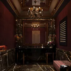 This dramatic powder room concept is wrapped in dark, veined marble and deep red textured walls. An ornate mirror and chandelier add to the opulent, moody atmosphere, creating an unforgettable experience.