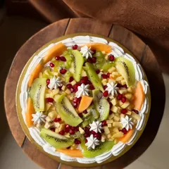 A top-down view of my fruit cake extravaganza. It's generously topped with kiwi, pomegranate, apple, and cantaloupe for a vibrant and healthy treat.