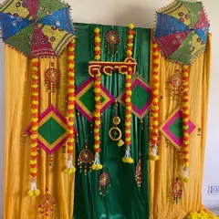 A vibrant Haldi or Mehendi backdrop using colorful drapes, marigold garlands, kites, and traditional Rajasthani umbrellas.