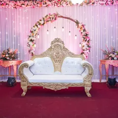 A close-up of the wedding stage decor, highlighting the ornate white and gold sofa where the bride and groom will be seated.